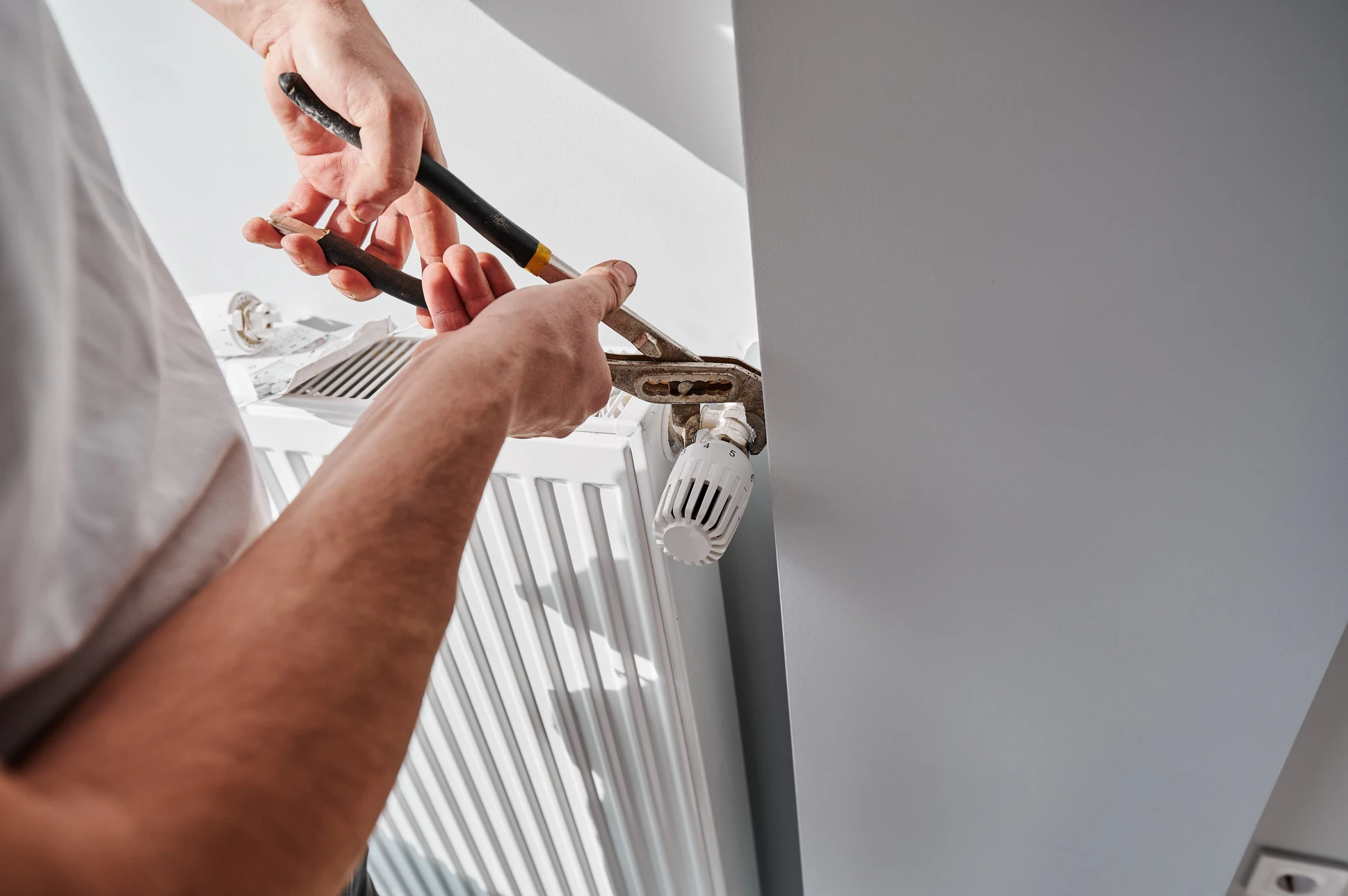 Intérieur résidentiel, technicien en plomberie-chauffage réparant un radiateur blanc à ailettes