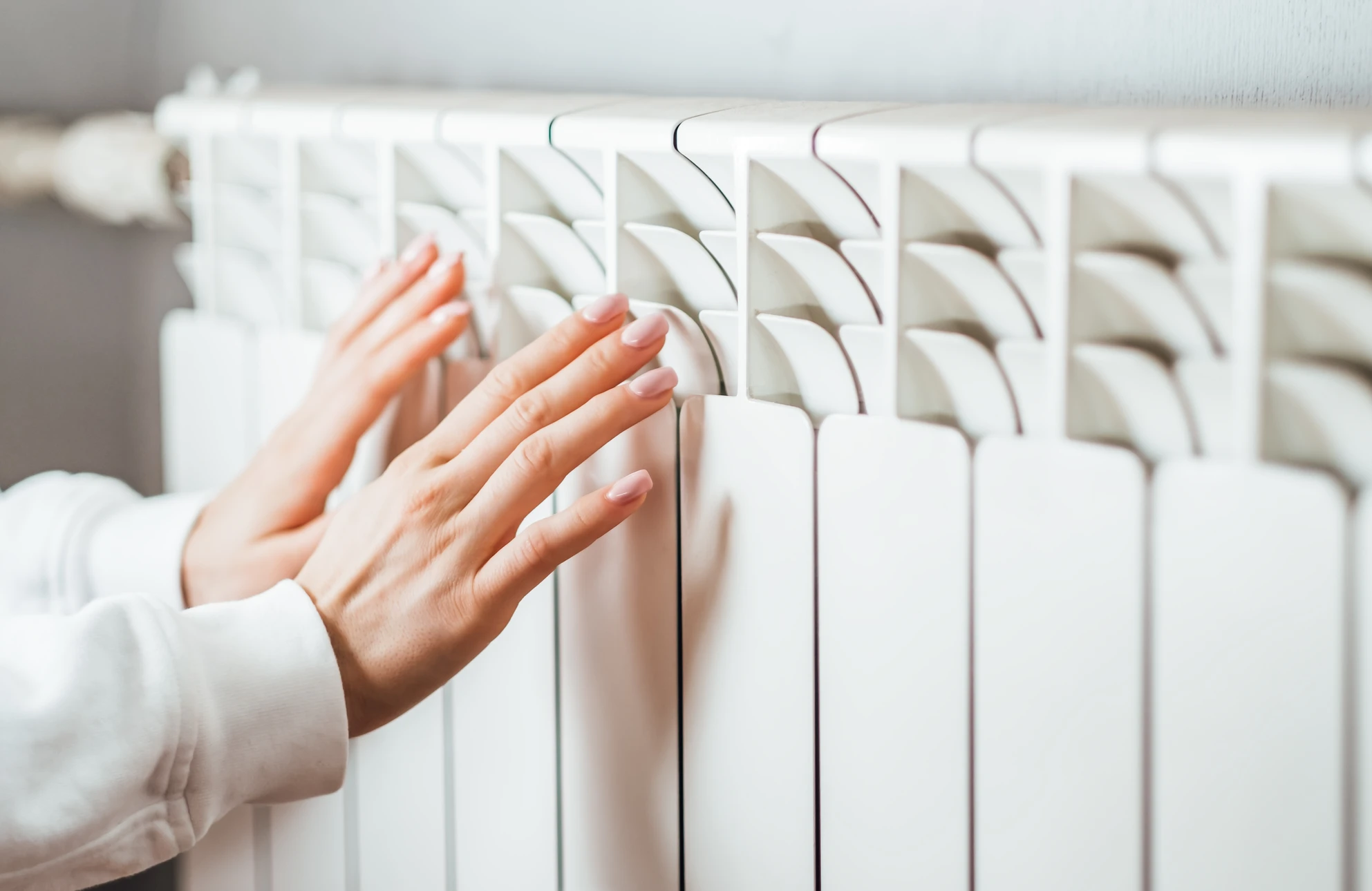 Technicien en combinaison rouge mesure un radiateur blanc avec un mètre ruban dans un intérieur résidentiel moderne