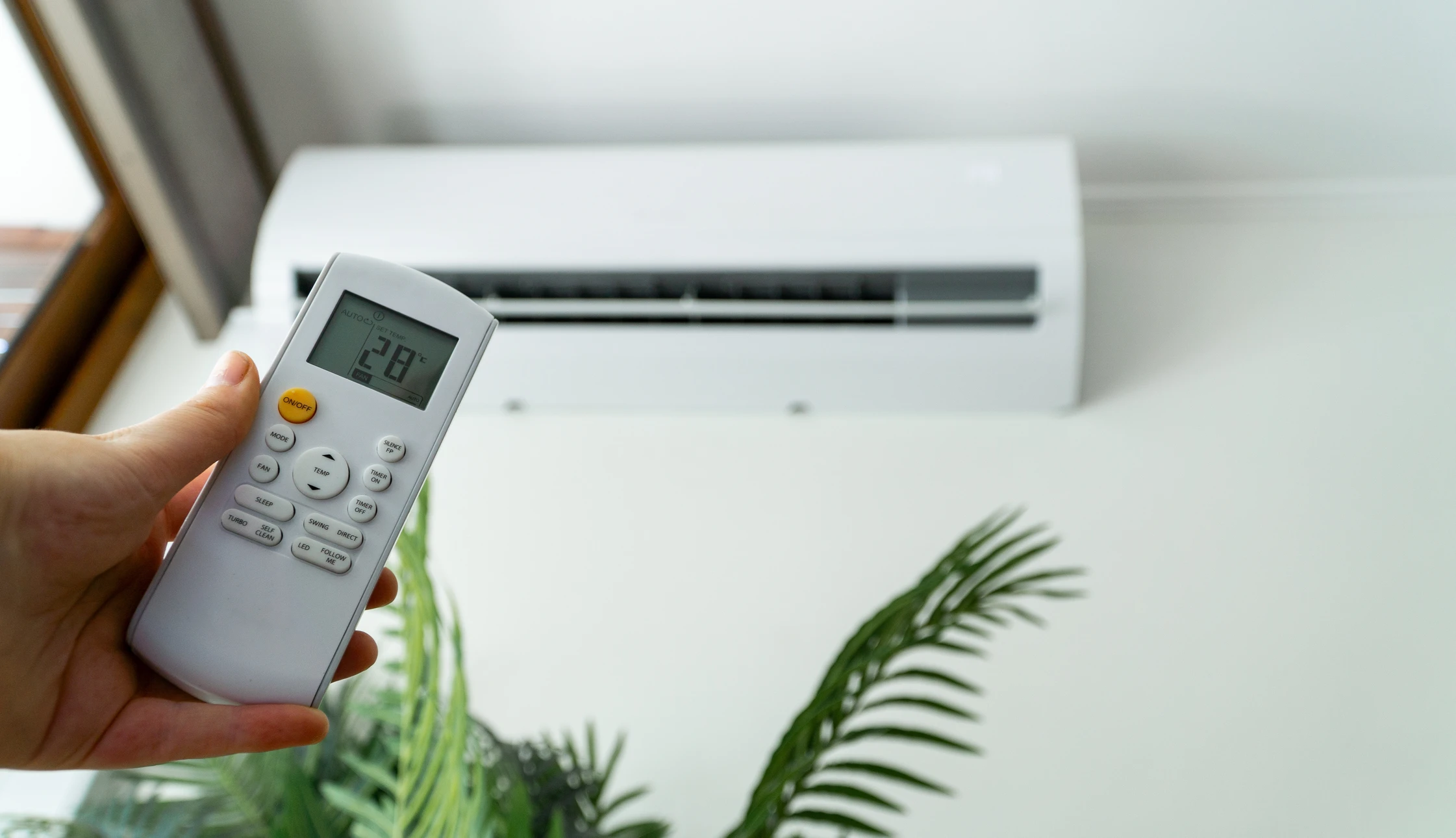 Un technicien en chemise grise installe ou répare une climatisation murale dans un intérieur moderne